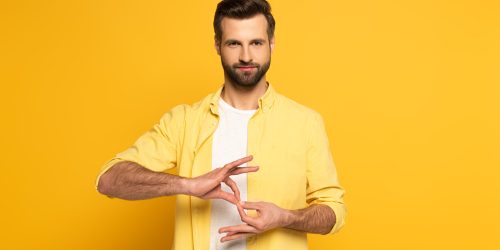 Handsome man showing interpretation sign in deaf and dumb language on yellow background Diplomado en interpretación de lenguas exóticas para eventos multiculturales